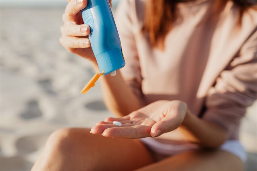 Person squeezing sunscreen lotion into a hand on the beach